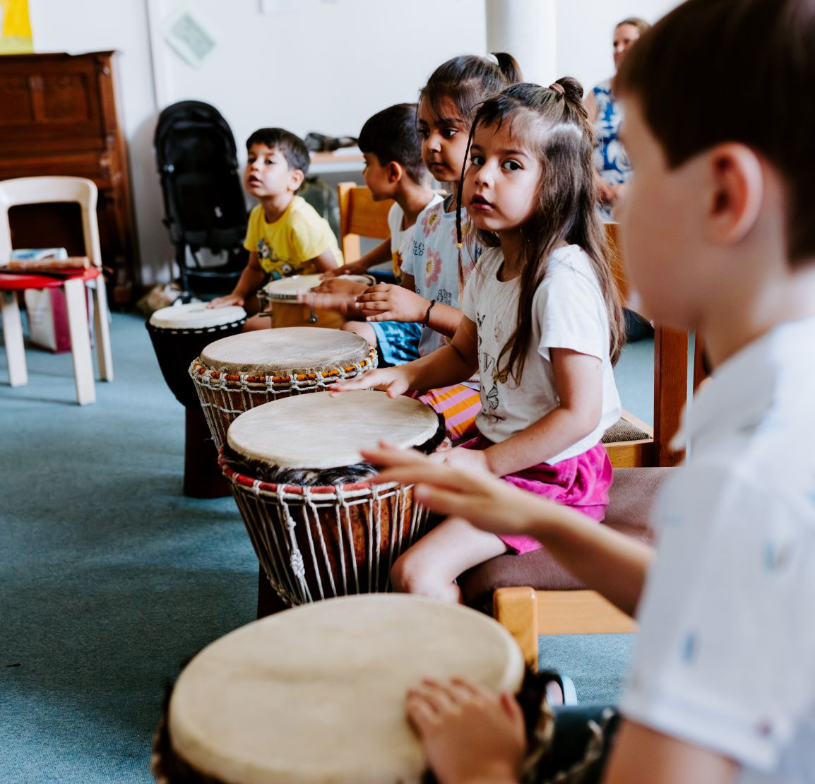Mehrere Kinder sitzen in einer Reihe und trommeln.