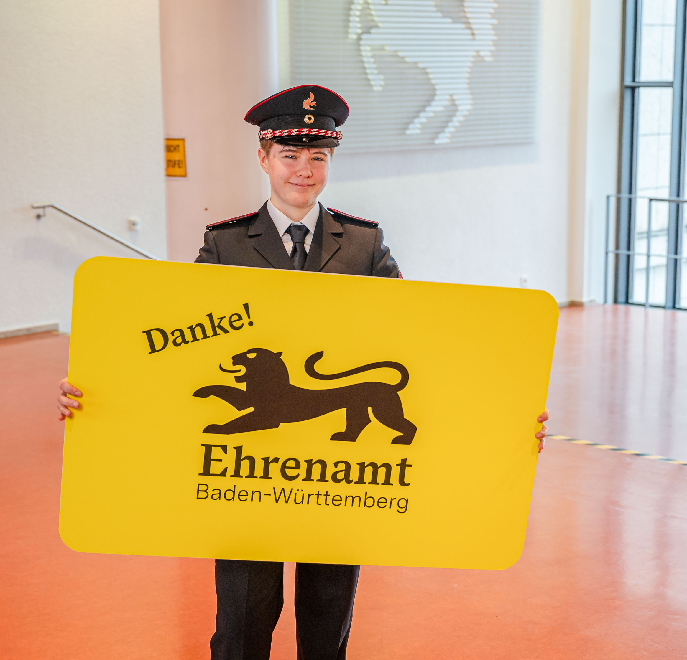 Eine junge Frau in Feuerwehruniform hält in der der Hand eine große gelbe Karte mit der Aufschrift "Danke! Ehrenamt Baden-Württemberg"