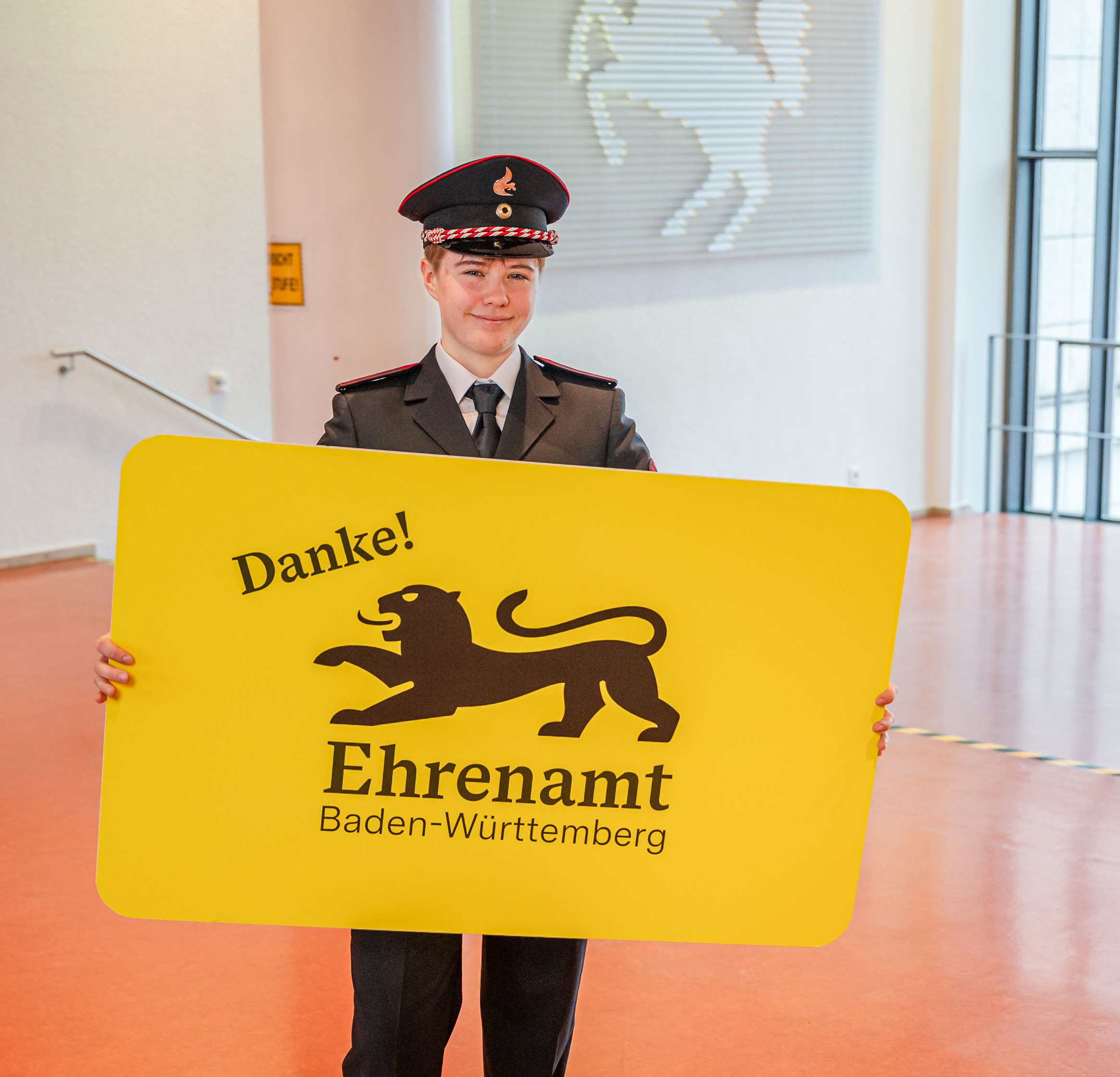 Eine junge Frau in Feuerwehruniform hält in der der Hand eine große gelbe Karte mit der Aufschrift "Danke! Ehrenamt Baden-Württemberg"
