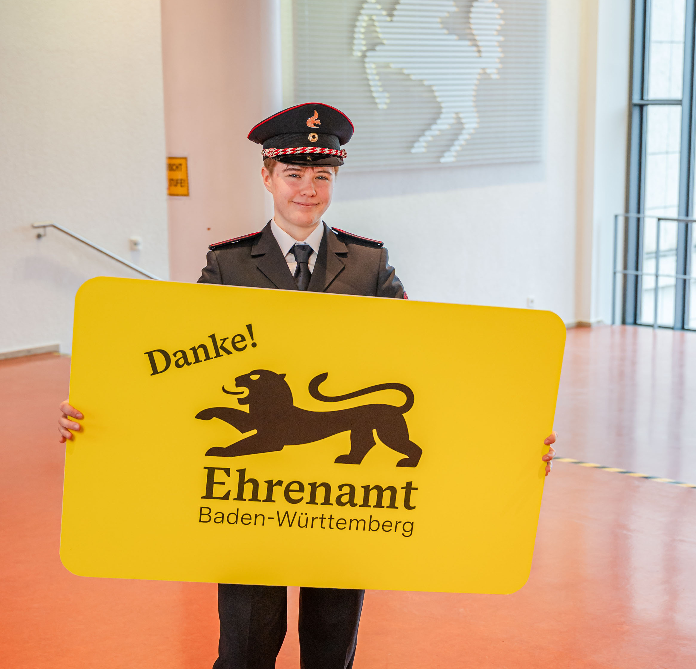 Eine junge Frau in Feuerwehruniform hält in der der Hand eine große gelbe Karte mit der Aufschrift "Danke! Ehrenamt Baden-Württemberg"