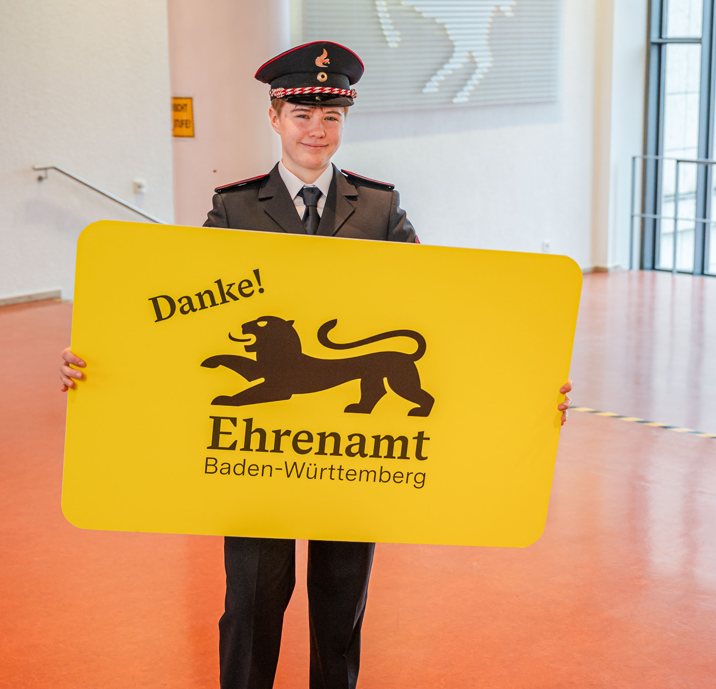 Eine junge Frau in Feuerwehruniform hält in der der Hand eine große gelbe Karte mit der Aufschrift "Danke! Ehrenamt Baden-Württemberg"