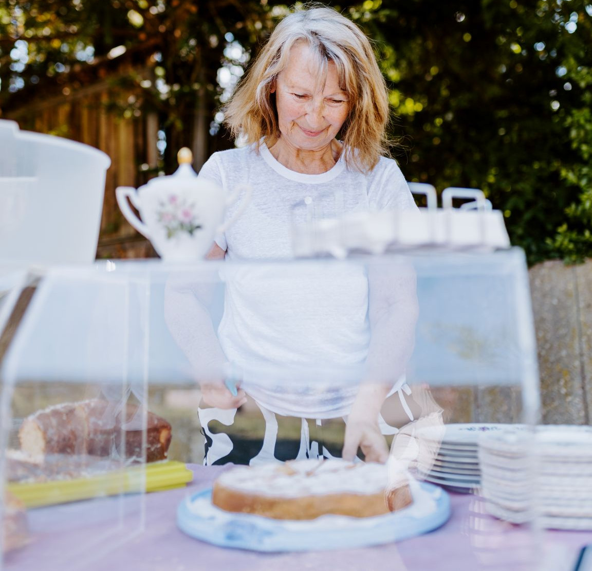 Eine Frau im mittleren Alter steht vor einem Kuchen und lächelt. 